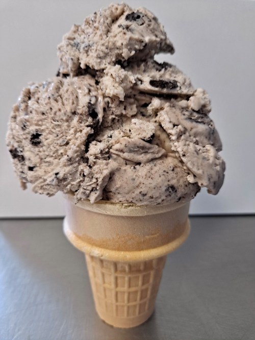 A tall ice cream cone filled with cookies and cream ice cream, topped with generous scoops.