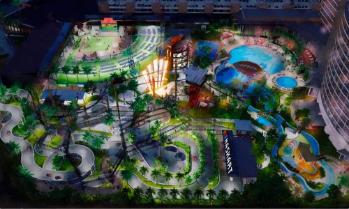 Aerial view of a vibrant amusement park featuring rides, pools, and green spaces, illuminated at night.