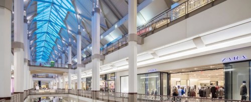 A spacious shopping mall interior with high ceilings, large windows, and storefronts, including Zara.