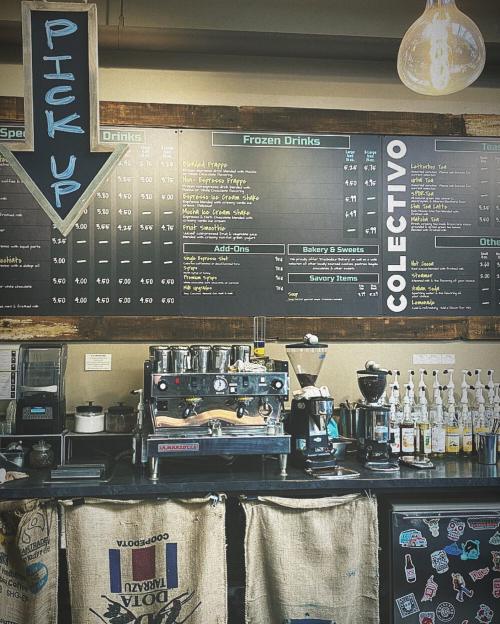 A coffee shop menu board displaying drinks, prices, and a coffee machine, with a "Pick Up" sign above.