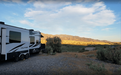 A camper parked in a scenic landscape with mountains and a blue sky at sunset.