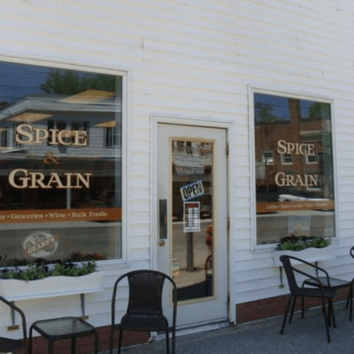 Exterior of a store named "Spice & Grain," featuring large windows and an open sign, with chairs outside.