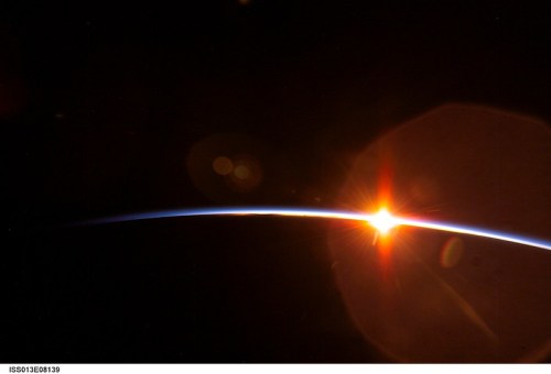 A stunning view of Earth’s horizon with a bright sunrise illuminating the edge of the planet against a dark background.