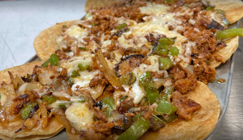 Close-up of nachos topped with seasoned meat, melted cheese, and sautéed peppers and onions on crispy tortillas.