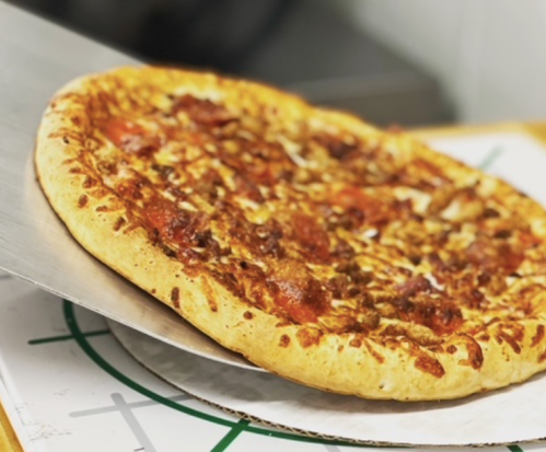A freshly baked pizza with pepperoni and cheese being lifted from a wooden surface.