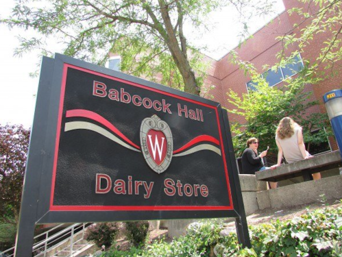 Sign for Babcock Hall Dairy Store at the University of Wisconsin, with people sitting nearby.