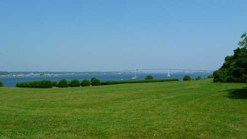 A serene landscape featuring a green field, calm water, and a distant bridge under a clear blue sky.