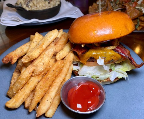 A juicy burger with bacon and cheese, served with crispy fries and a side of ketchup on a gray plate.
