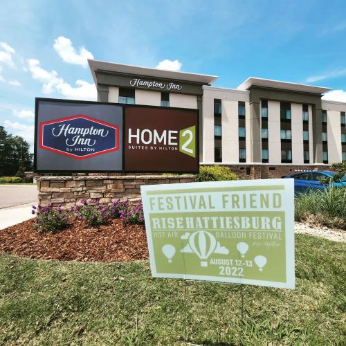 Sign for Hampton Inn and Home2 Suites by Hilton, with a festival sign for the Rise Hattiesburg Hot Air Balloon Festival.