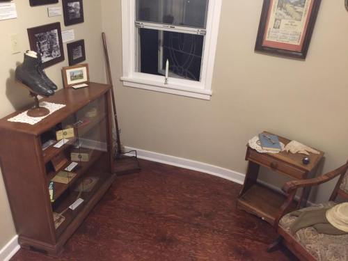 A cozy room corner featuring a display case, a vintage chair, and a window, with historical items on the walls.