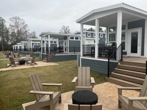 Row of modern cabins with porches, surrounded by green grass and outdoor seating areas. Overcast sky in the background.