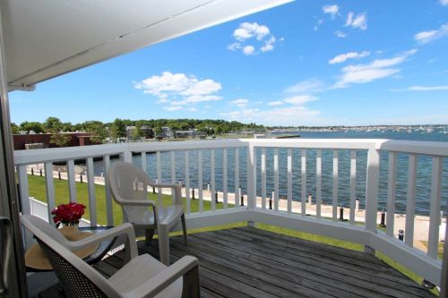 A scenic view from a balcony overlooking a calm waterfront with blue skies and green grass.