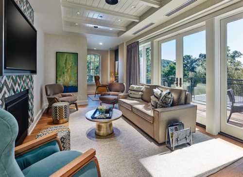 Modern living room with large windows, comfortable seating, a coffee table, and a view of greenery outside.