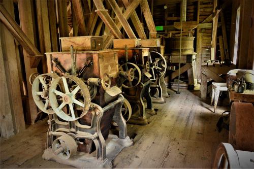 Two vintage machines with large wheels in a rustic wooden interior, surrounded by various tools and equipment.