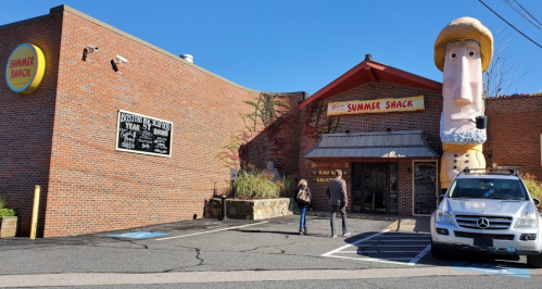 A restaurant called "Summer Shack" with a large inflatable figure outside and two people approaching the entrance.