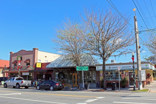 A charming street scene featuring shops with festive decorations and bare trees under a clear blue sky.