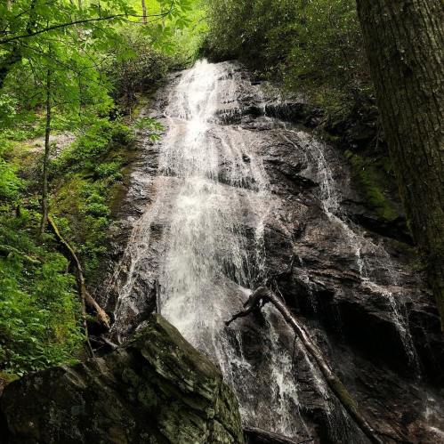A serene waterfall cascading down rocky terrain, surrounded by lush green foliage and trees.