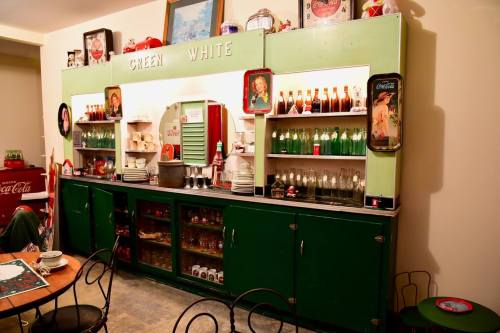 A vintage soda fountain display with green and white cabinetry, featuring glass bottles and nostalgic decor.