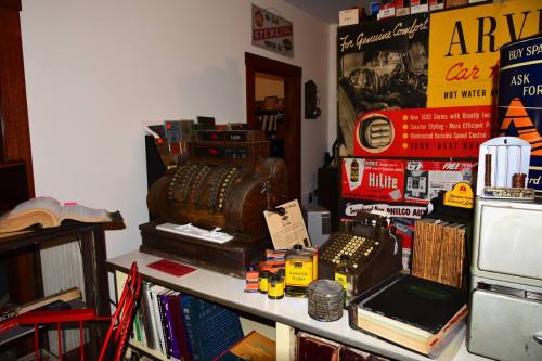 A vintage cash register on a table surrounded by old books and various retro advertisements and items.