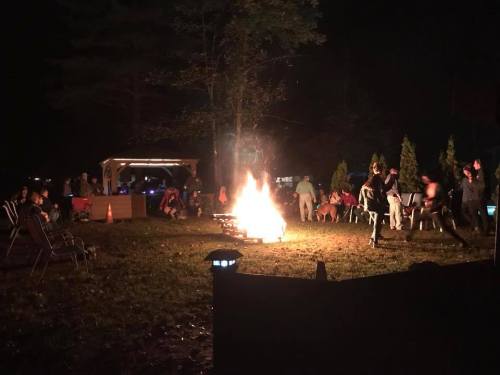 A lively campfire gathering at night, with people sitting around the fire and enjoying the outdoors.