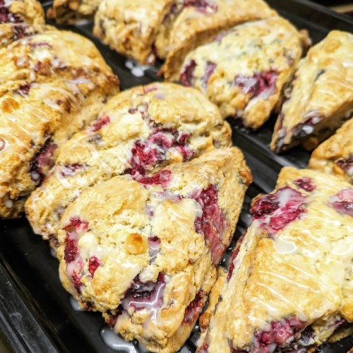 Freshly baked scones with a berry filling, drizzled with a sweet glaze, arranged on a black tray.