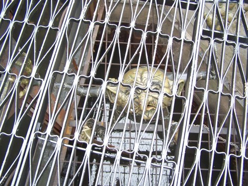 A close-up of a decorative metal grate revealing a sculpted face beneath it.