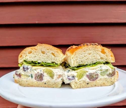 A sandwich on a plate, filled with creamy chicken salad, grapes, and lettuce, served on a toasted bun.
