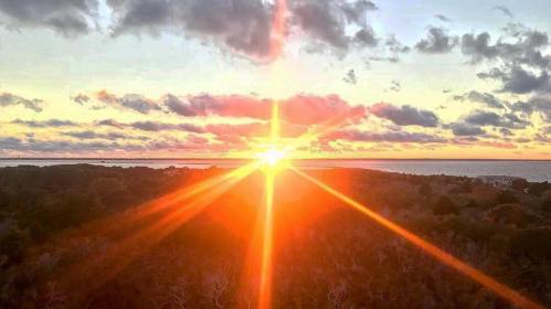 A vibrant sunset over a landscape, with rays of light shining through clouds and reflecting on the water.