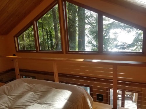 Cozy interior with large triangular windows overlooking a forested area and water, featuring wooden accents.