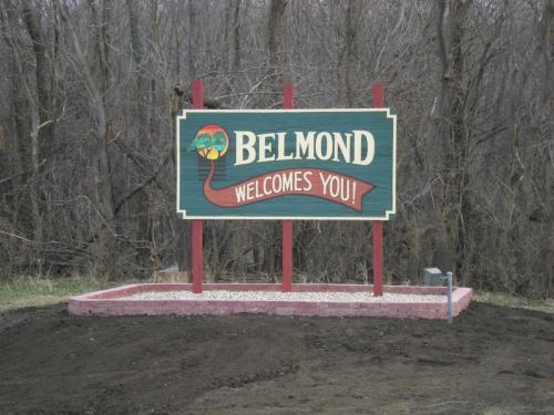 Sign reading "Belmond Welcomes You!" surrounded by trees, set on a gravel base.