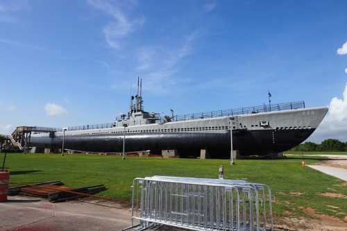 A large submarine displayed on land, surrounded by green grass and blue sky, with a viewing platform nearby.