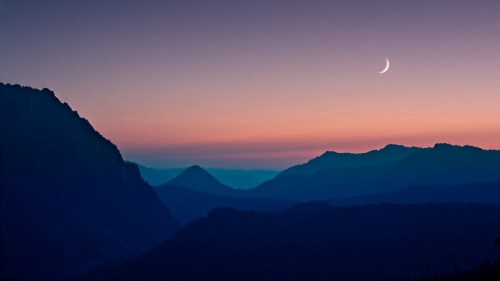 A serene twilight landscape with mountains silhouetted against a gradient sky and a crescent moon.