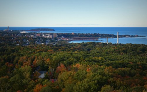 A scenic view of a coastal town surrounded by colorful autumn foliage and a calm blue lake.