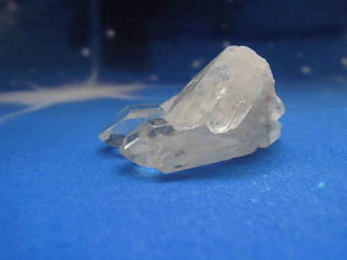 A clear crystal fragment resting on a blue background with a starry pattern.