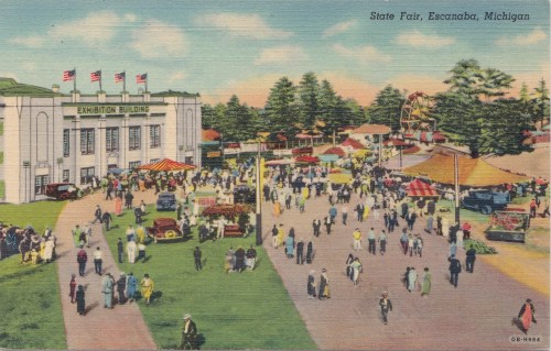A vintage postcard of the State Fair in Escanaba, Michigan, featuring crowds, booths, and the Exhibition Building.