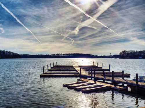 A serene lake scene with a wooden dock, reflecting sunlight, and wispy clouds in a blue sky.