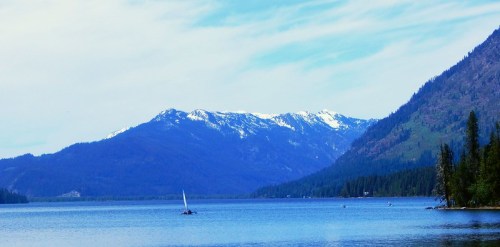 A serene lake surrounded by mountains, with a sailboat gliding across the water under a blue sky.
