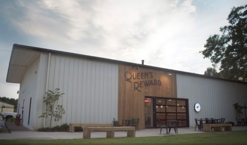 Exterior of Queen's Reward building with wooden accents, benches, and a cloudy sky in the background.
