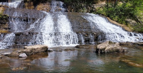 A serene waterfall cascading over rocks into a clear pool, surrounded by lush greenery.