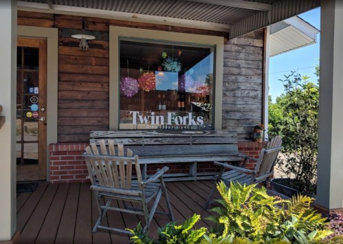 A cozy outdoor seating area with wooden chairs and a table in front of a shop window that reads "Twin Forks."