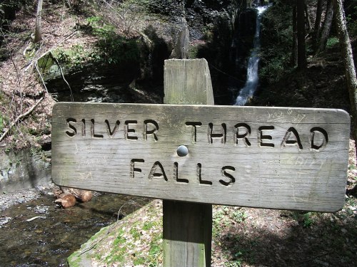 A wooden sign reading "Silver Thread Falls" in a forested area near a waterfall and stream.