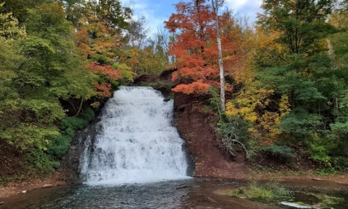 A picturesque waterfall surrounded by vibrant autumn foliage in a serene forest setting.