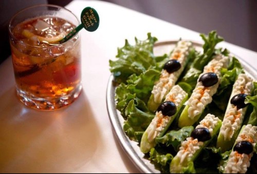 A plate of lettuce wraps filled with creamy filling and olives, alongside a glass of a dark cocktail with ice.