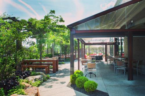 Outdoor dining area with wooden tables, greenery, and a modern structure under a clear blue sky.