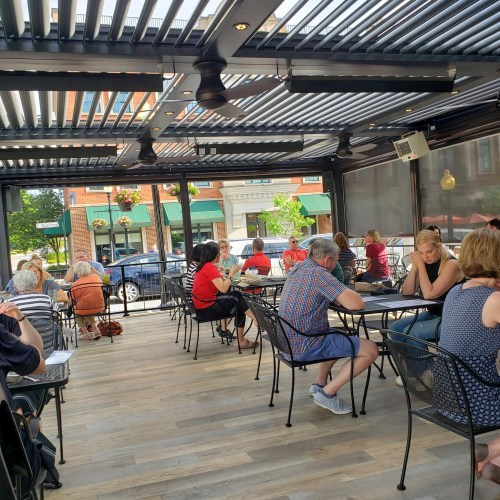 A bustling outdoor dining area with patrons seated at tables, enjoying their meals under a retractable roof.