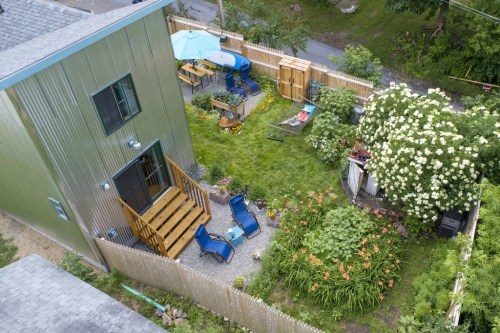 Aerial view of a backyard with a green house, garden, patio furniture, and lush greenery.