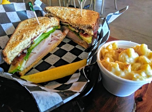 A sandwich with turkey, lettuce, and bacon, served with a side of creamy macaroni and cheese and a lemon wedge.