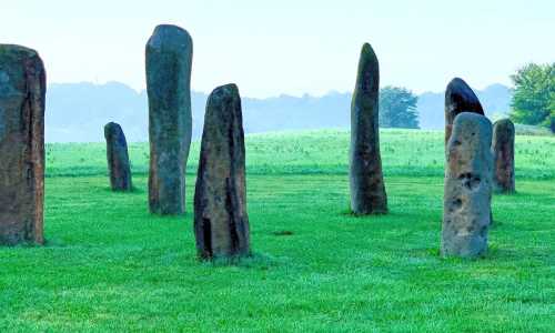 A circle of tall, ancient stone monoliths standing in a grassy field under a clear sky.