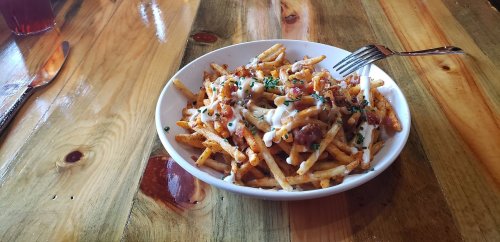 A bowl of loaded fries topped with cheese, bacon, and green onions on a wooden table.