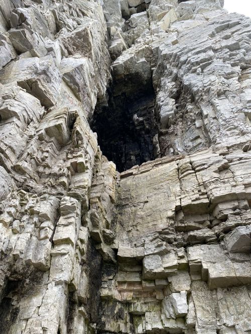 A close-up view of a rugged rock formation with layered, textured stone and a dark crevice.